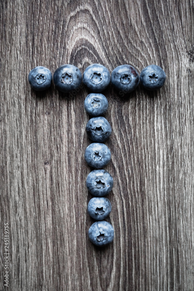 Wall mural letter t laid out of blueberry berries on a wooden background