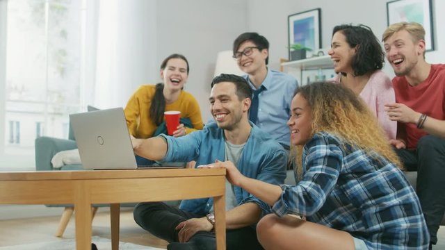 Diverse Group of Friends Use Laptop in the Living Room. Happy Beautiful Girls and Guys Doing Live Streaming. They Have Fun and Laugh.