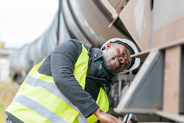 African American railroad engineer wearing safety equipment (helmet and jacket) checking gear train