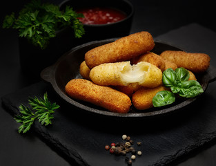 Delicious breaded mozzarella cheese sticks in a pan against a dark background