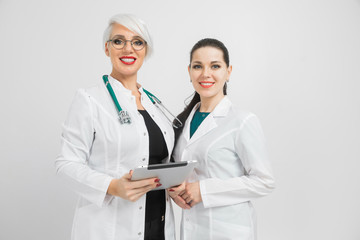 Two female doctors with tablet and sheet with analysis in hands isolated on white background