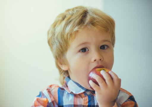 Cute toddler child eating red apple in hands on the day of valentine. Little blond boy with red delicious apple on white background. Child portrait with food.