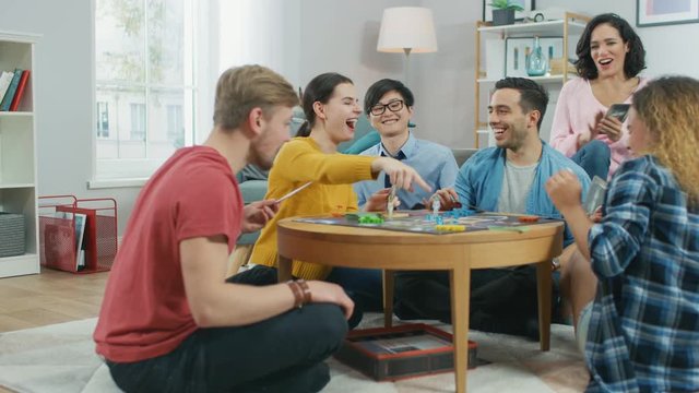 Diverse Group of Guys and Girls Playing in a Strategic Board Game with Cards and Dice. Reading Cards and Laughing. Friends Having Fun. Cozy Living Room in a Daytime