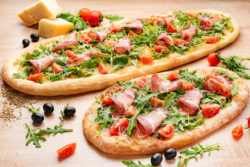 Flatbread pizza garnished with fresh arugula on wooden pizza board