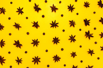 Star anise and allspice in lines with hard shadow on yellow background, flat lay image.