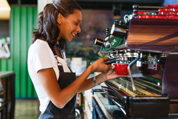 Plakat Side view of a smiling female barista making coffee at a cafe