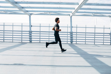Fototapeta na wymiar Side view of a young male runner exercising outdoors, wearing black sports clothes