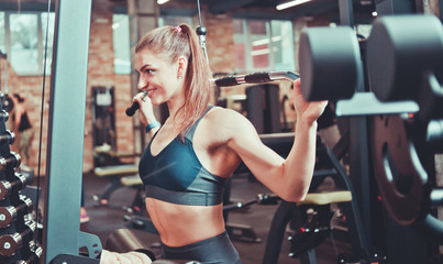 Athlete woman training her back, arms and shoulders with exercise machine in a gym, sport concept