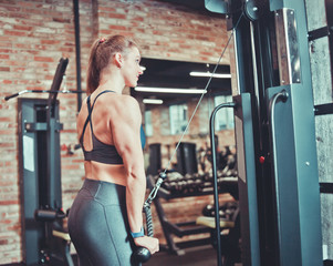 Fitness young woman in sport wear with perfect body doing triceps exercise with ropes in the gym.