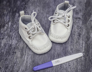 Fototapeta na wymiar Waiting for a baby. White baby shoes and pregnacy test