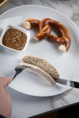 Mann isst Münchener Weißwurst mit Messer und Gabel, süßen Senf und Brezel und löst Wurst...