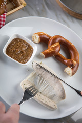 Mann isst Münchener Weißwurst mit Messer und Gabel, süßen Senf und Brezel und löst Wurst richtig aus Pelle