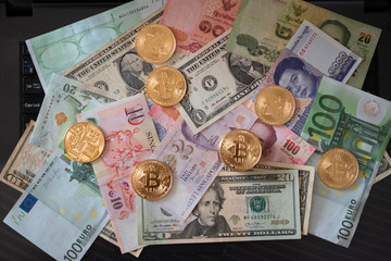 On the laptop keyboard are various banknotes, coins and bitcoins.