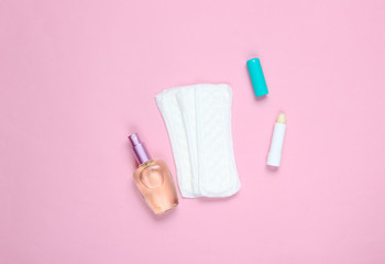 Women's beauty and hygiene products on a pink pastel background. Perfume bottle, hygienic lipstick, pads. Flat lay style.