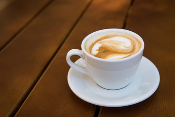 Tasse Cappuccino Kaffee mit Milchschaum auf Holztisch draußen im Biergarten