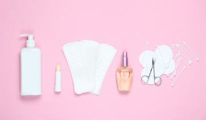 Women's beauty and hygiene products on pink pastel background. Perfume bottle, hygienic lipstick, pads, bottle cream,nail scissors. Flat lay style, top view.