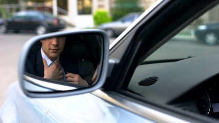 Businessman straightening shirt, ready for meeting, reflection in wing mirror