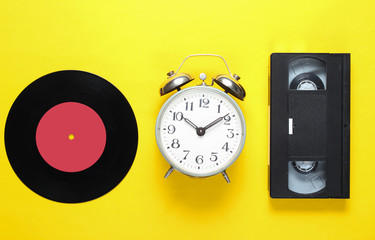 Retro vinyl record, old alarm clock, video tape on a yellow background. 80s. Top view. Minimalism