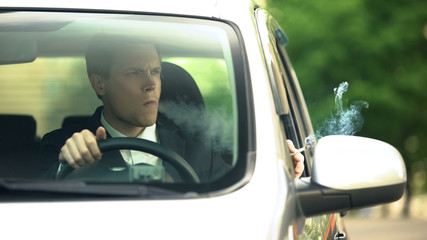 Relaxed businessman smoking thoughtfully inside car in traffic, office break