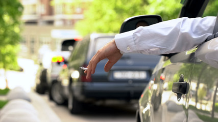 Man smoking in auto, dumping cigarette ash on street, stuck in traffic jam