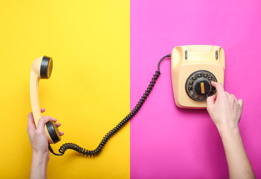 Woman picks up the number of the rotary phone and holds the handset on a colored paper background. Top view, minimalism