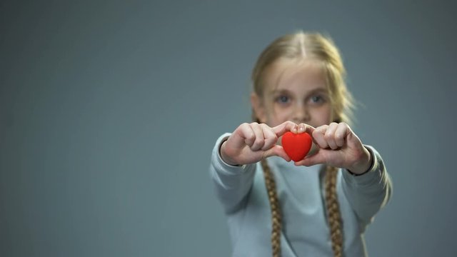 Smiling Little Girl Showing Heart Figure Into Camera, Love And Kindness Concept