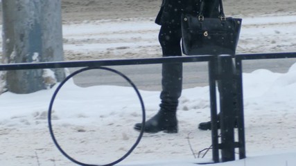 Woman in winter leather boots walking on sidewalk in city during snowfall. Slow motion. Closeup on legs.