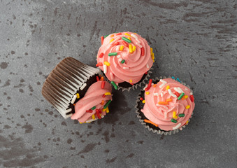 Three pink frosted chocolate cupcakes on a gray background top view.