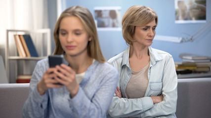 Daughter with smartphone in hands ignoring her mom, indifference, puberty age