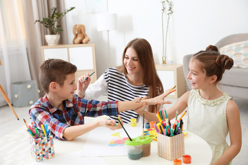 Young woman and children having fun with paints at table indoors