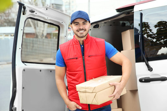 Young courier with parcels near delivery van outdoors