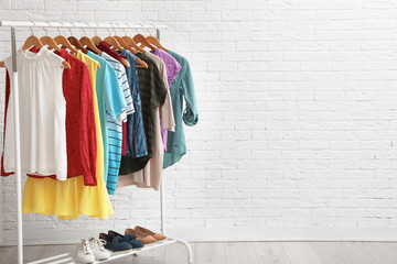 Wardrobe rack with stylish clothes and shoes near brick wall indoors. Space for text - obrazy, fototapety, plakaty