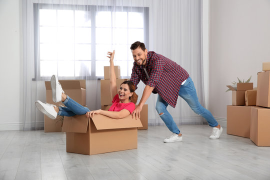 Happy couple playing with cardboard box in their new house. Moving day