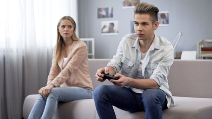 Offended girl looking at her boyfriend who indifferently playing video games © motortion