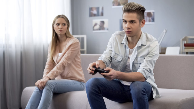 Offended girl looking at her boyfriend who indifferently playing video games