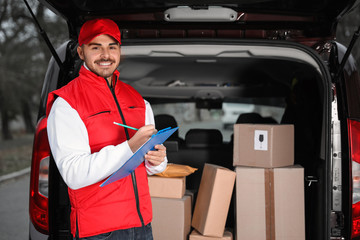 Deliveryman with clipboard near van with many parcels outdoors