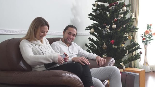 Handsome man gives present to his wife and shows credit card. Woman excited of the gift. A child with his new toy runs up to his parents. Family celebrates xmas at home.