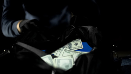 Male bandit looking at money bag stolen from city bank, robbery, criminality