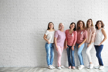 Group of women with silk ribbons near brick wall, space for text. Breast cancer awareness concept