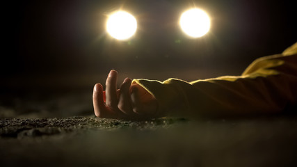 Car headlighting unconscious victim, lying on road after accident, crime