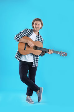 Young man playing acoustic guitar on color background