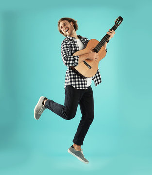 Young man playing acoustic guitar on color background
