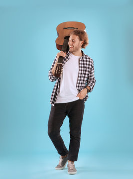 Young man with acoustic guitar on color background