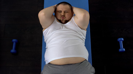 Persistent overweight man doing sit-ups lying on floor, genetic predisposition