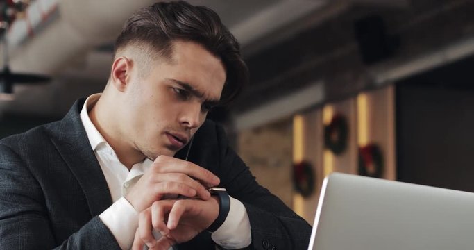 Stressed young businessman with laptop working at cafe. He talking with boss talk phone and writes the notes to the notebook. Hard business, people, deadline and technology concept
