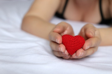 Declaration of love, woman holding red knitted heart in hands. Sexy girl in underwear lying on the...
