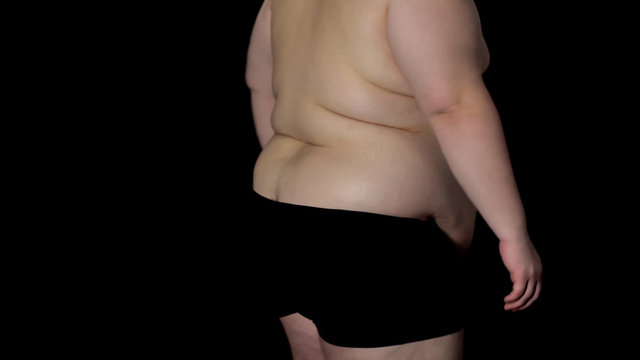 Back view overweight man on dark background, lack of activity, health problems