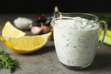 Glass jug of Tzatziki cucumber sauce with ingredients on table. Space for text