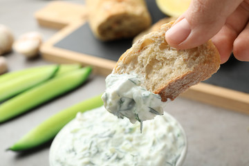 Woman dipping bread in cucumber sauce on blurred background. Traditional Tzatziki