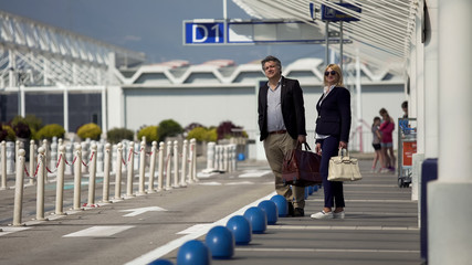 Foreign tourists with bags waiting for shuttle bus near airport terminal exit
